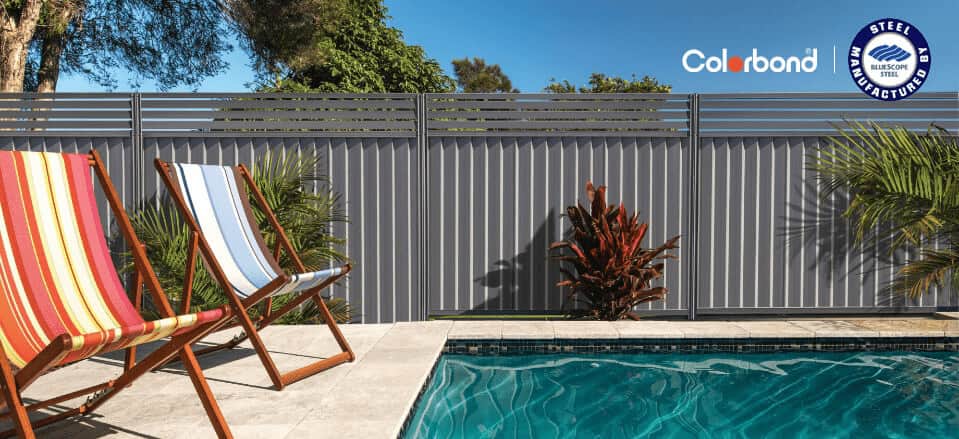 Outdoor swimming pool with deck chairs in front of a Charcoal coloured Colorbond fence.