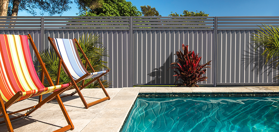 A backyard pool and deck chairs, with a Colorbond&reg; Steel Fence behind.
