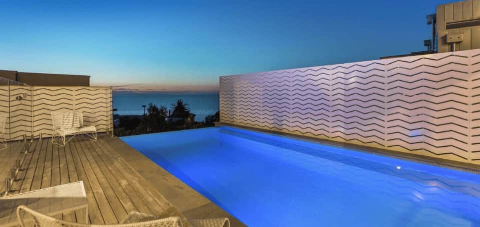 Outdoor deck and swimming pool surrounded by a laser cut zig-zag patterned privacy screen.