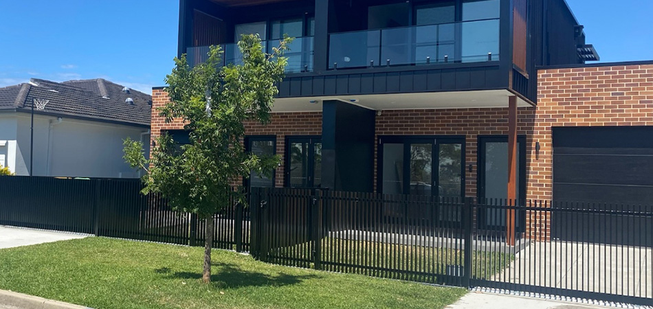 The front yard of a duplex, with alimunium batten fencing with a pedestrian and sliding gate installed.